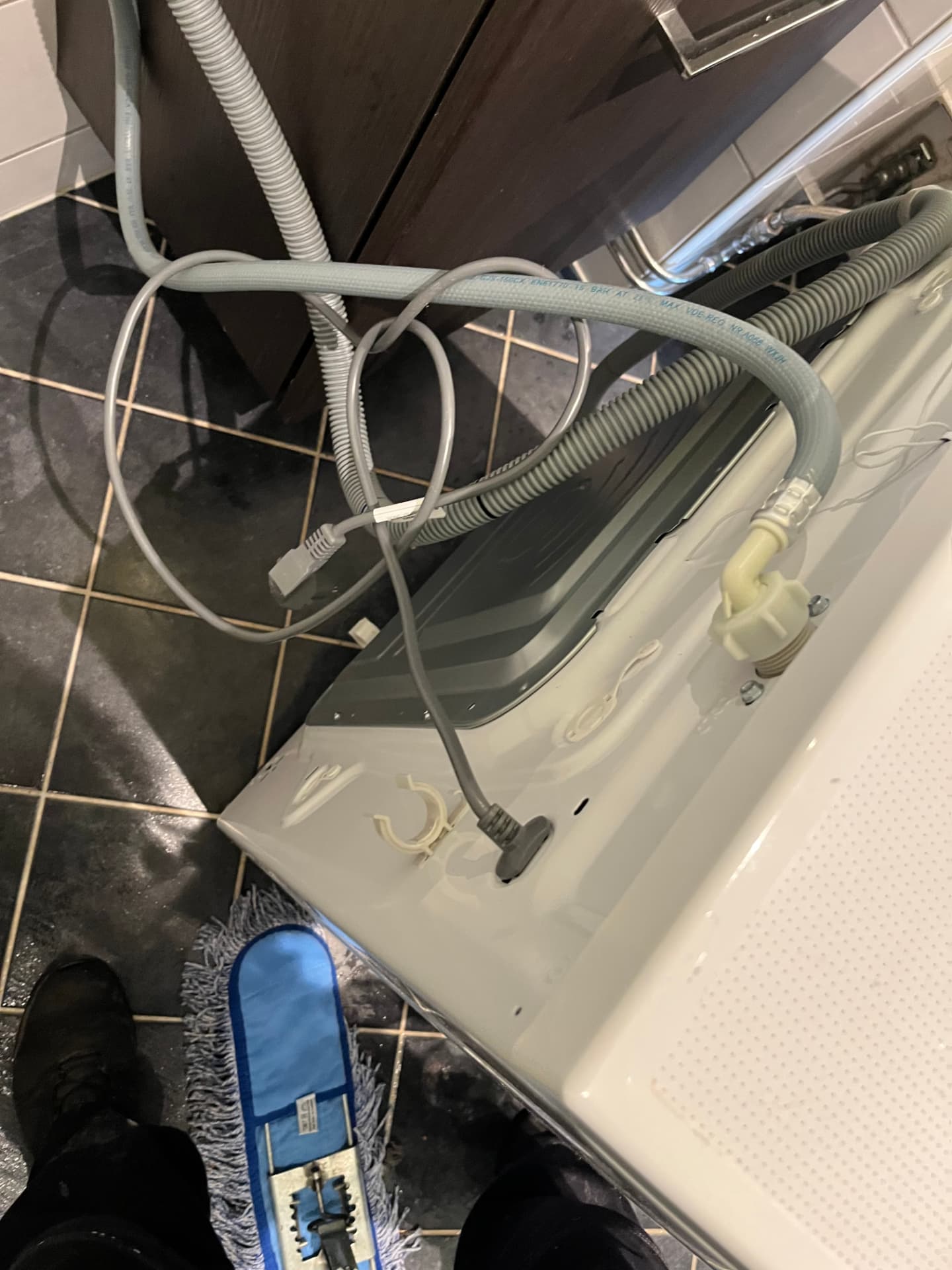 Vask av gulv bak vaskemaskin med slanger og kabler